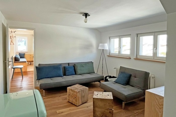 Der Wohnraum  Eingang und Herz der Ferienwohnung. Offen, klar, ruhig, gem�tlich. Mit Sofa und Sessel � beides l�sst sich im Handumdrehen in ein bequemes Schlafsofa und eine Ottomane verwandeln. Zwei massive W�rfel aus Tannenholz dienen als Hocker und / od